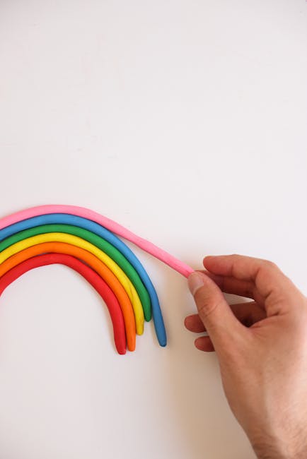 Hand arranging colorful clay rainbow on a white background.